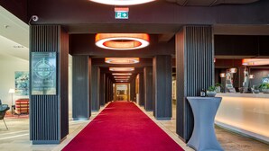 Un couloir d'hôtel avec un tapis rouge, un éclairage moderne et un comptoir d'accueil.