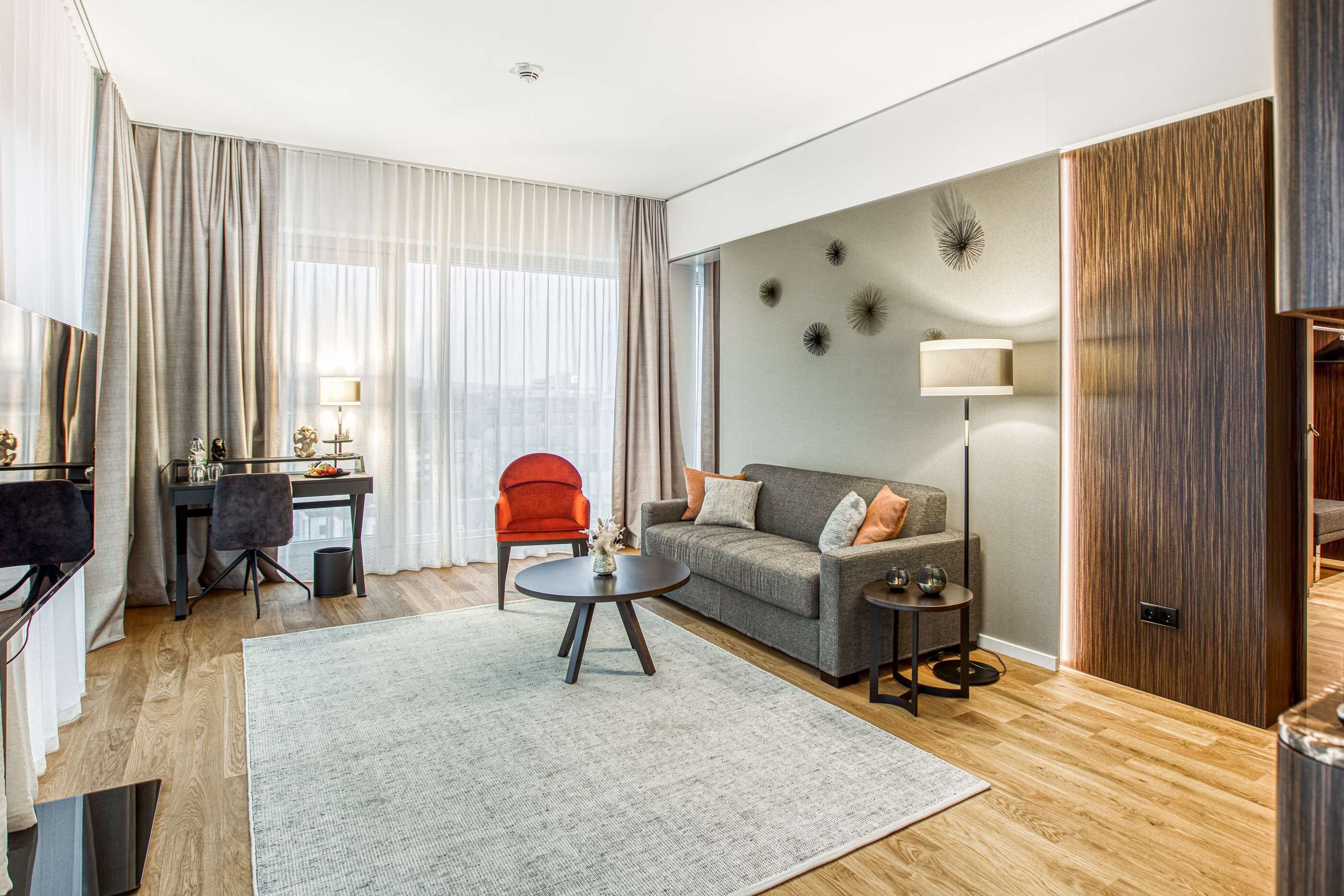A modern living room with a grey sofa, a red chair, a round coffee table, and a TV on a stand.
