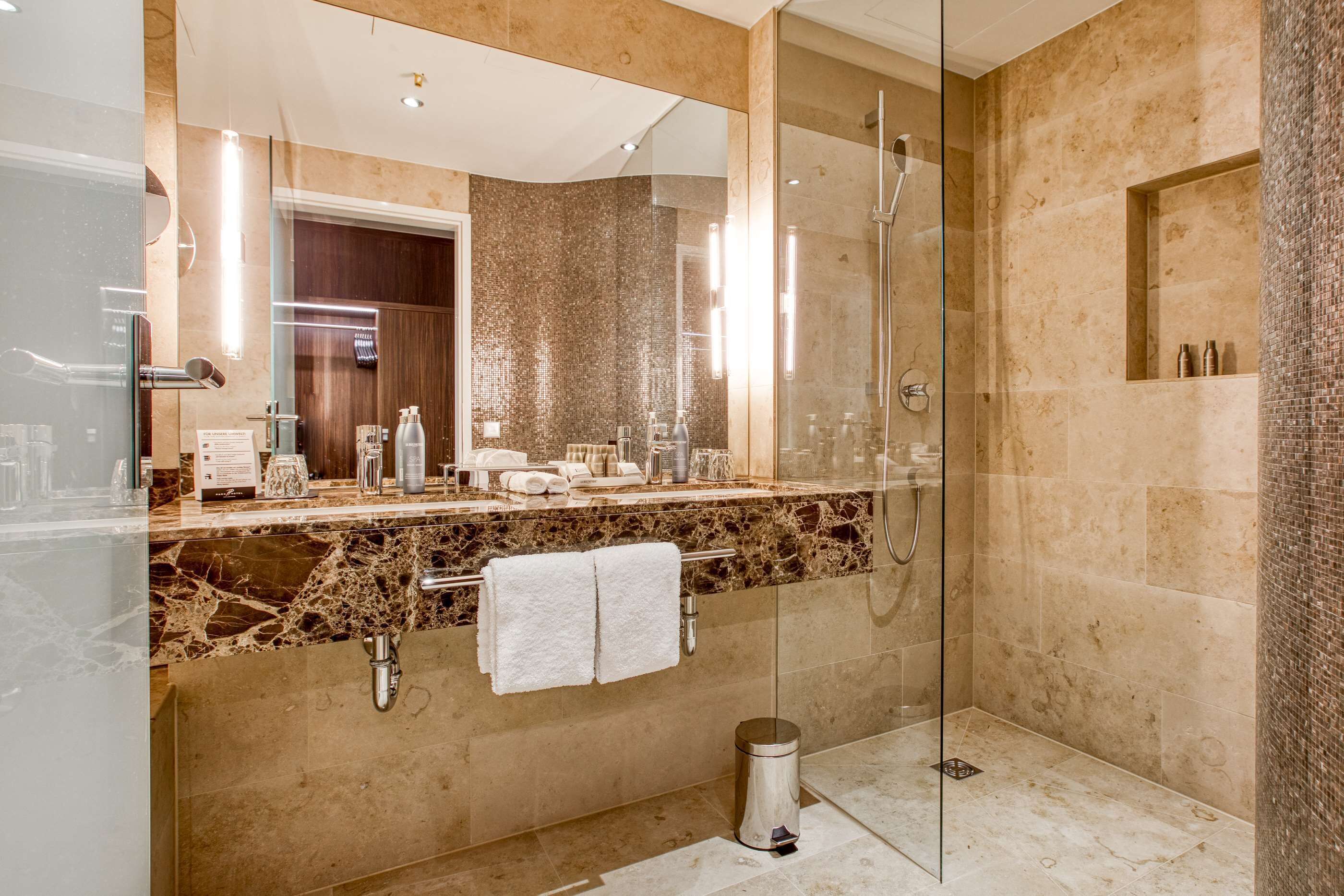 Une salle de bain moderne avec une douche à parois de verre, des comptoirs en marbre et un grand miroir.