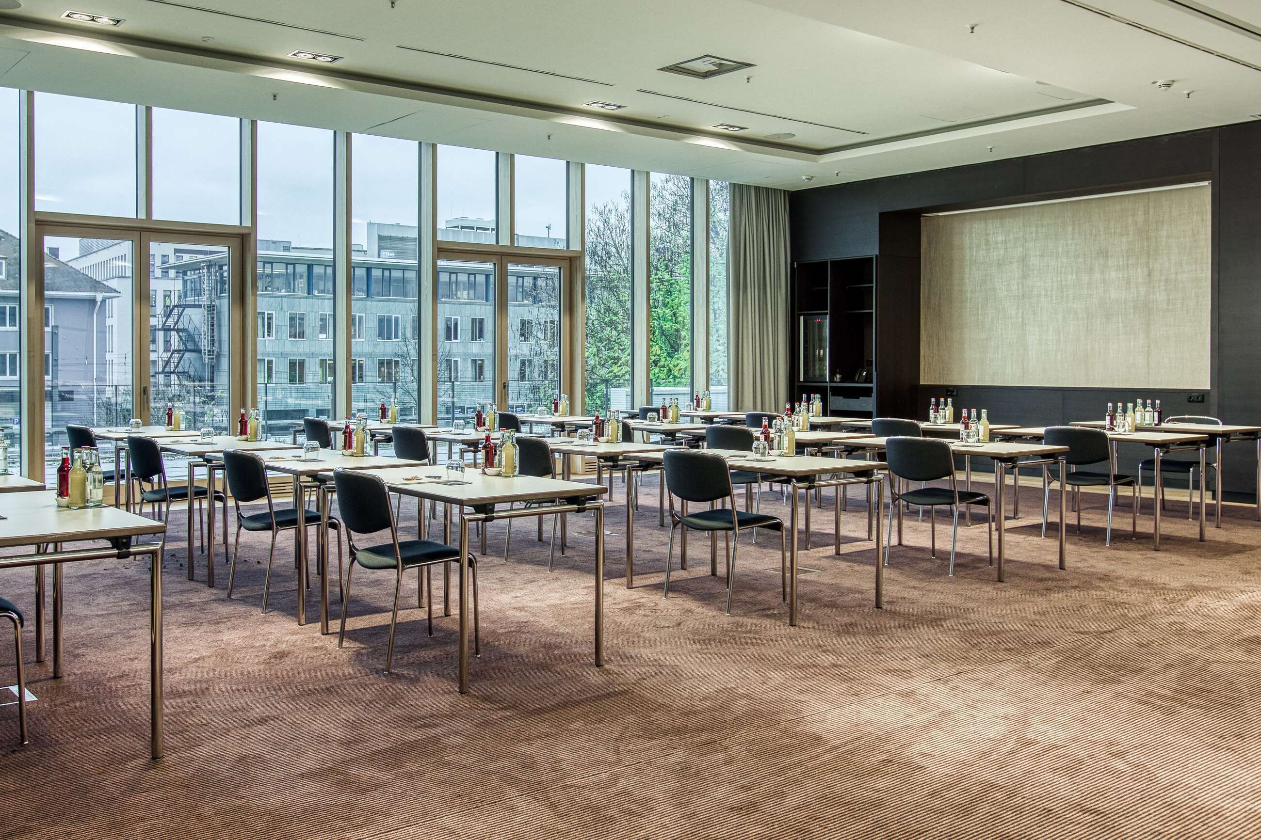 Un salón de conferencias con amplias ventanas, varias mesas y sillas, equipado con pantallas de presentación y diversos servicios.