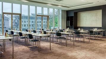 Un salón de conferencias con amplias ventanas, varias mesas y sillas, equipado con pantallas de presentación y diversos servicios.