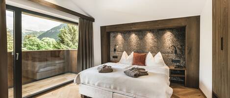 Un dormitorio moderno con una cama grande, un muro decorativo de piedra y vistas a zonas verdes a través de una puerta corredera.