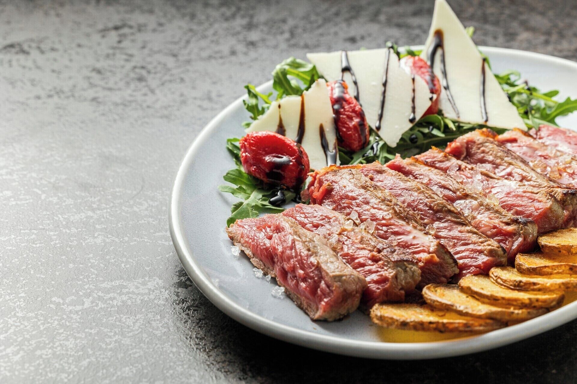 A plate with sliced steak, roasted potatoes, and a salad with cherry tomatoes and cheese.
