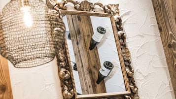 Ein Spiegel mit aufwendigem Rahmen, der zwei Weinflaschen und eine Pendelleuchte reflektiert.