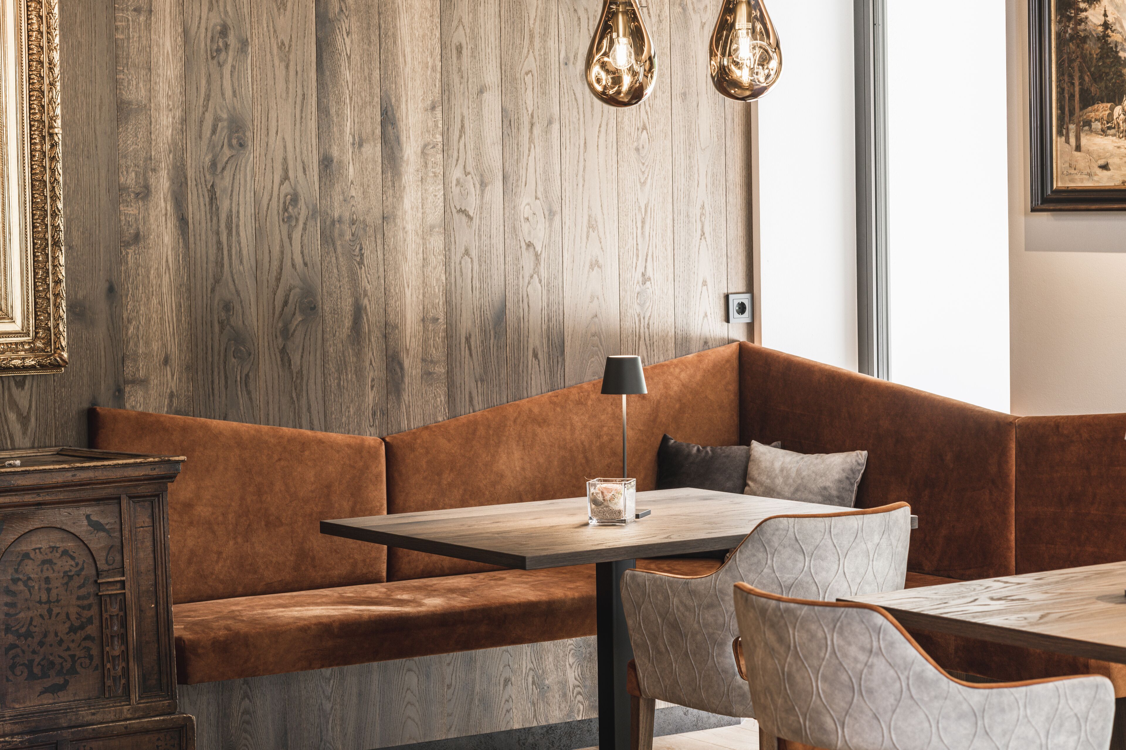 Un interior moderno con una pared de madera, un banco con cojines marrones, una mesa de madera y una lámpara.