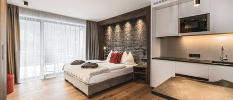 Una habitación de hotel moderna con una cama grande, una cocina integrada con microondas y una pared de acento de piedra.