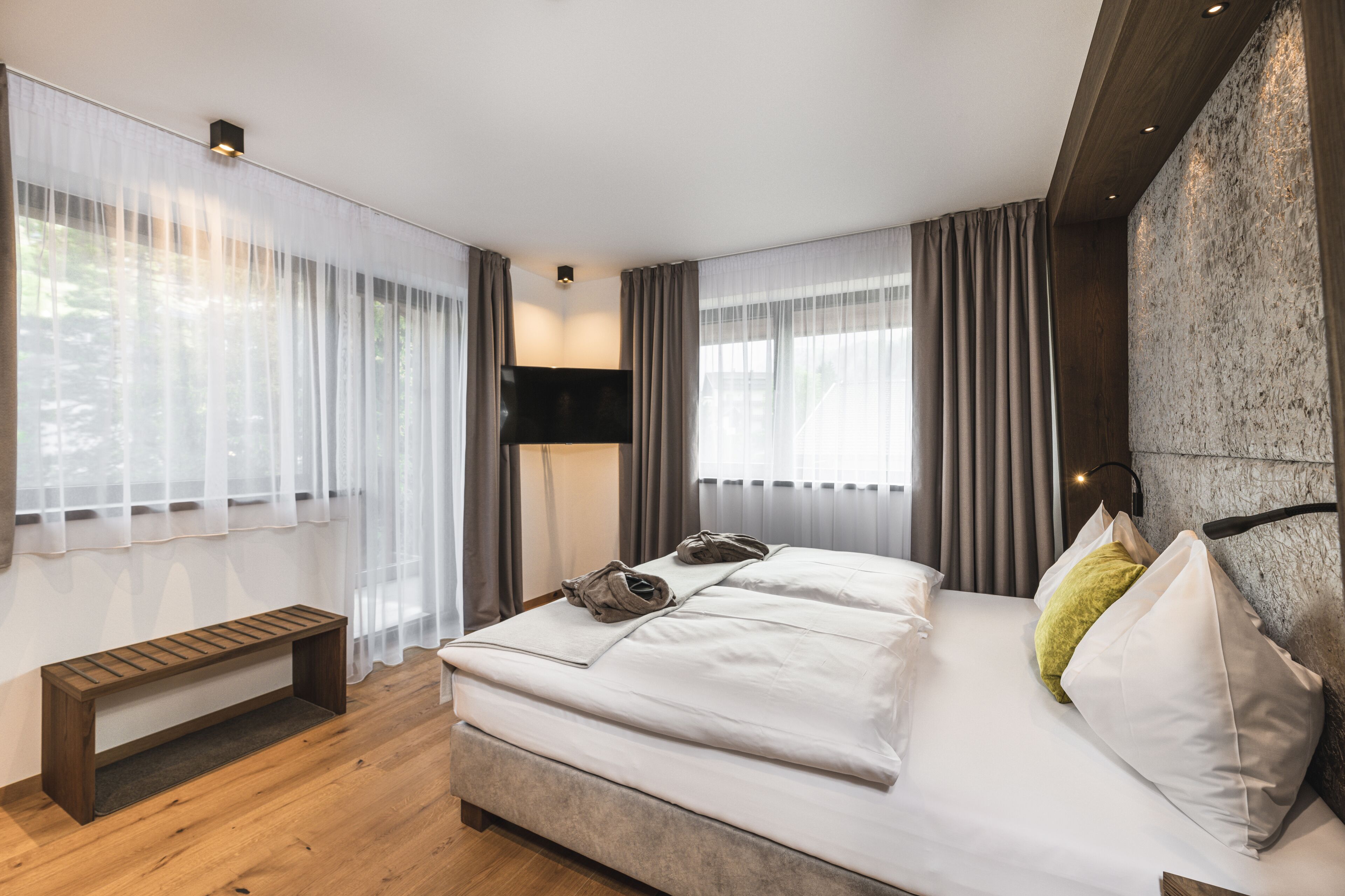 Una habitación de hotel moderna con una cama grande, un banco y un televisor de pantalla plana.