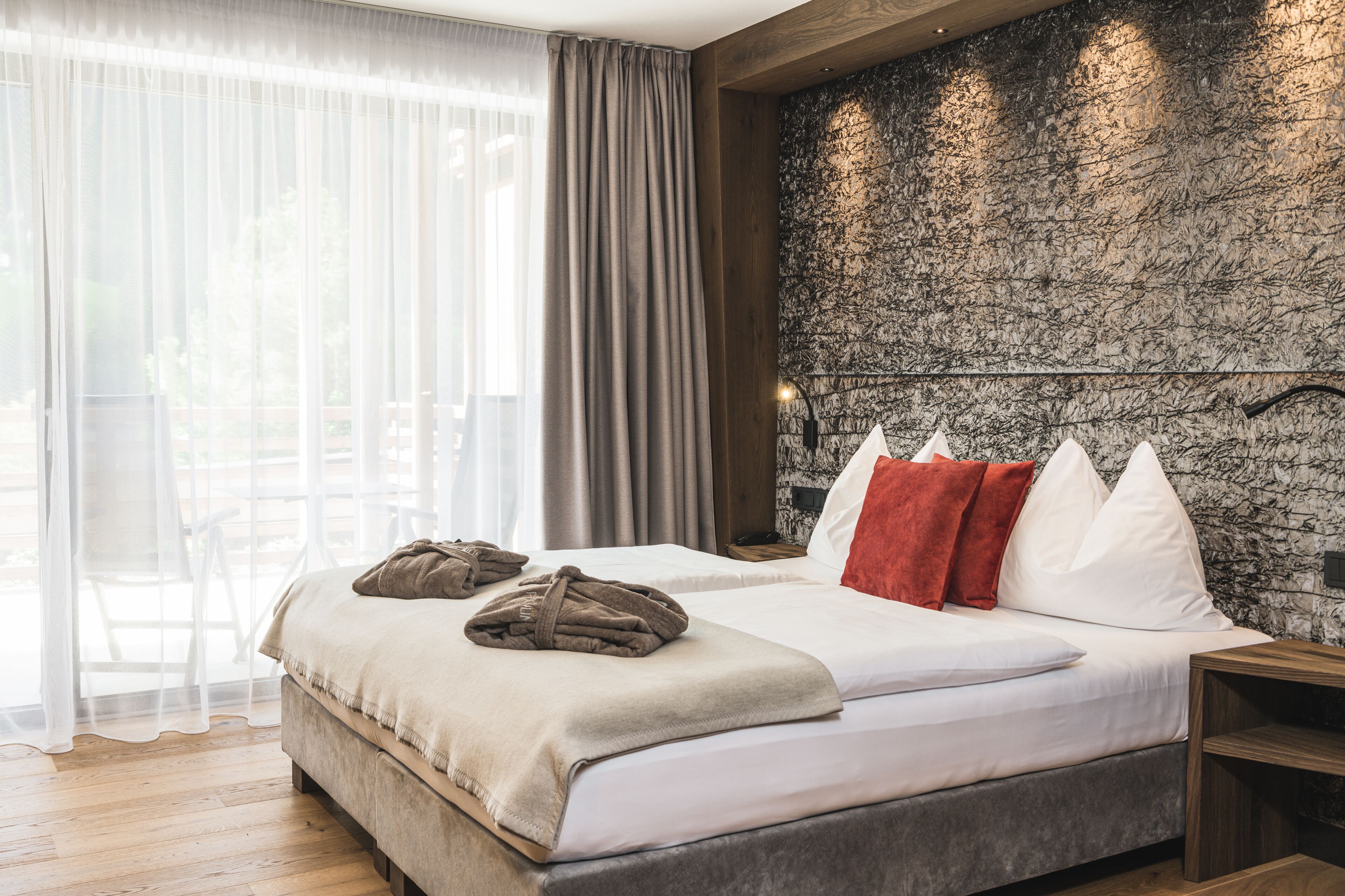 A bedroom with a large bed, wooden headboard, and a stone-textured wall.