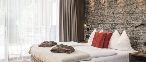 A bedroom with a large bed, wooden headboard, and a stone-textured wall.
