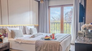 Una habitación de hotel moderna con una cama grande, un balcón con vistas y un escritorio pequeño con una lámpara.