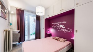 Un dormitorio moderno con una cama rosa, una pared de acento morada con texto motivacional, una ventana con cortinas y un radiador.