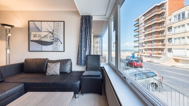 Una habitación de hotel moderna con un ventanal grande, un sofá de cuero negro, una mesita pequeña y vistas a la ciudad.