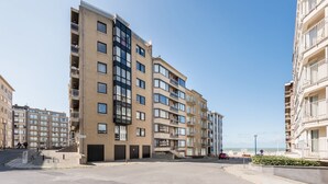 Un edificio residencial de varios pisos con balcones, un estacionamiento y vistas despejadas a la playa.