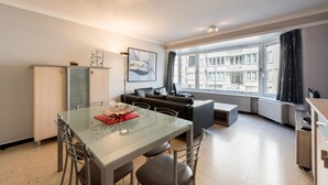Una sala de estar moderna con una mesa de comedor de vidrio, un sofá y un amplio ventanal con vistas a la ciudad.