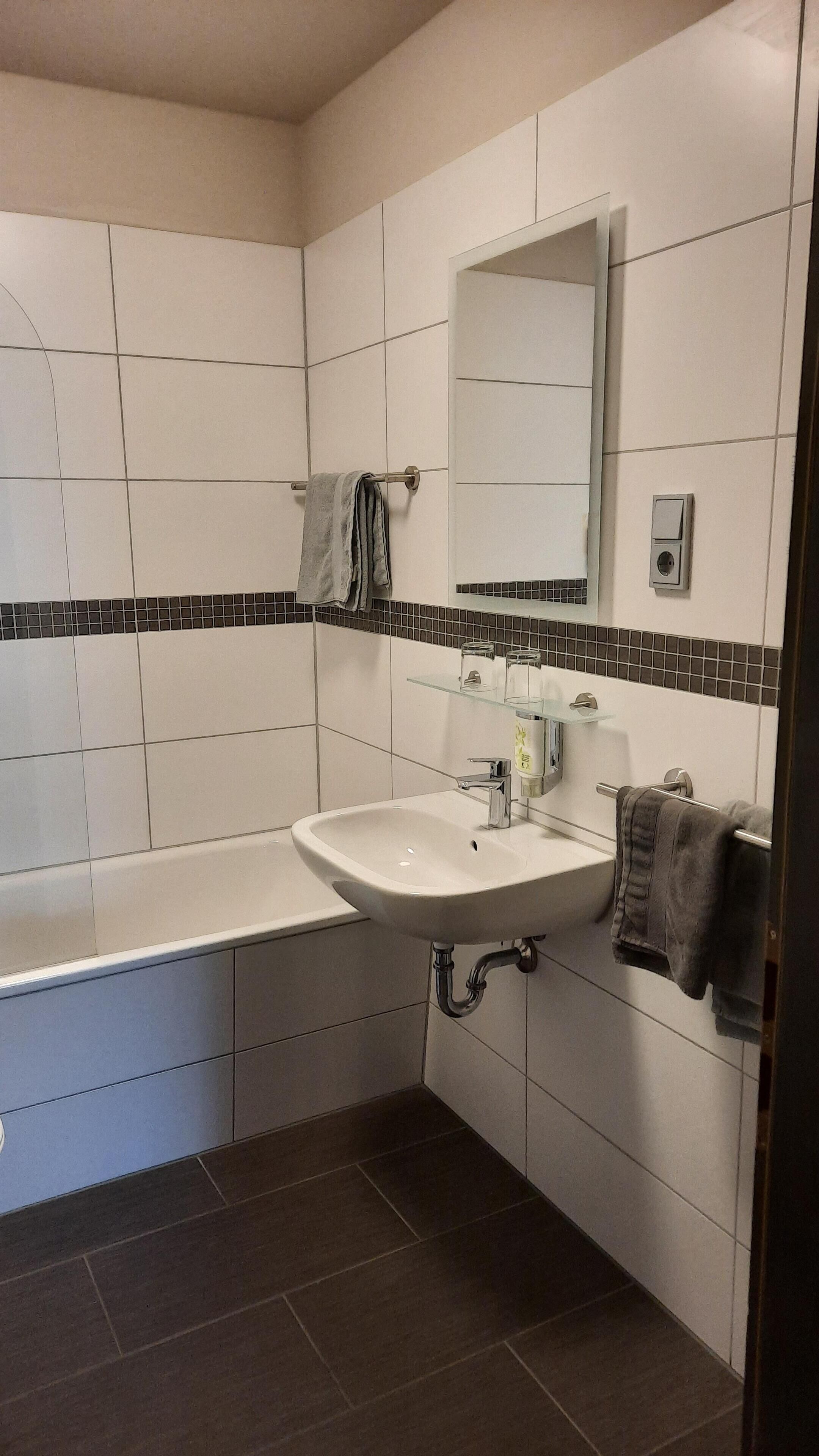 Un baño moderno con un lavamanos blanco, un espejo y una bañera.