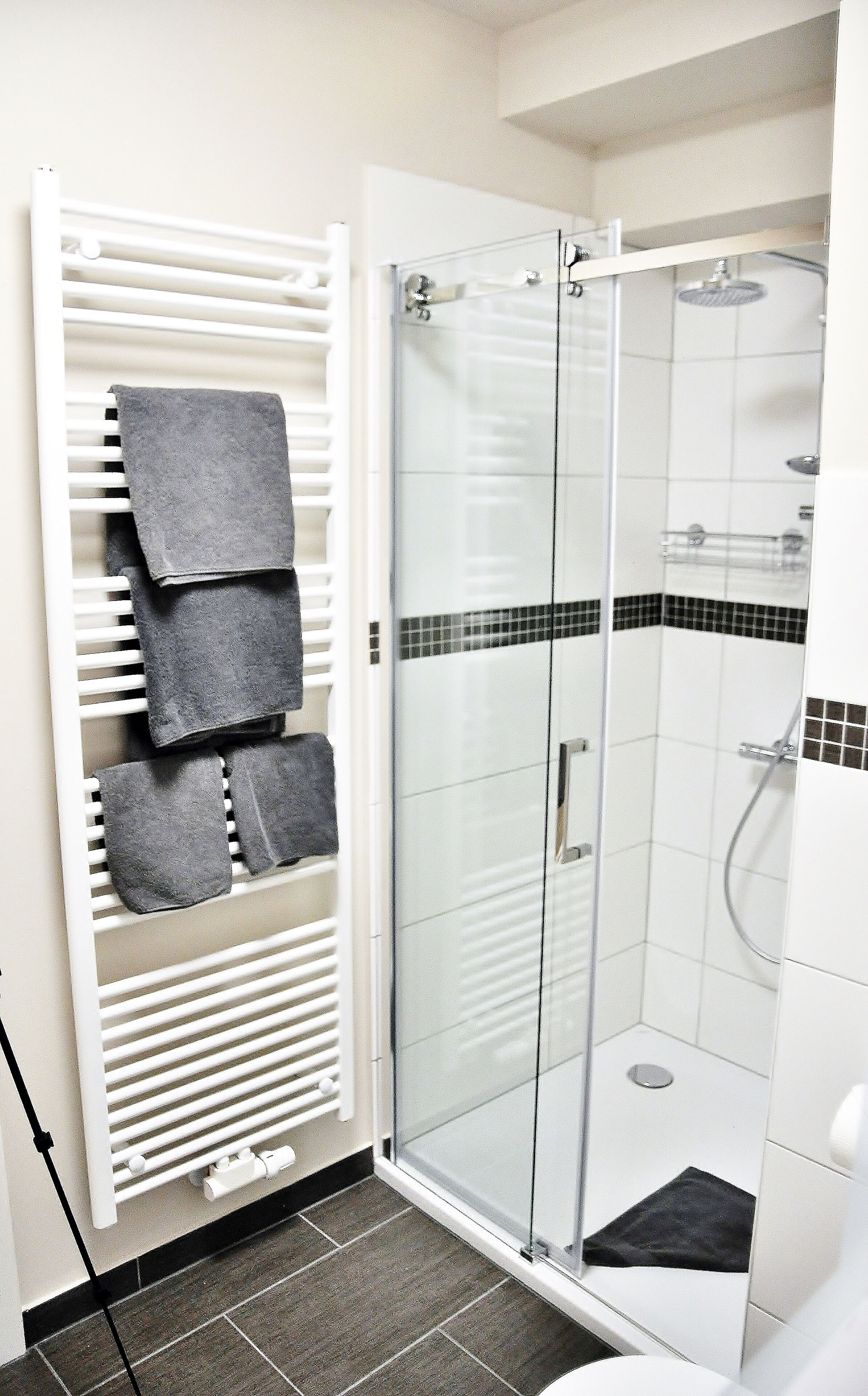 A modern bathroom with a glass-enclosed shower, a white towel rack with multiple towels, and a tiled floor.