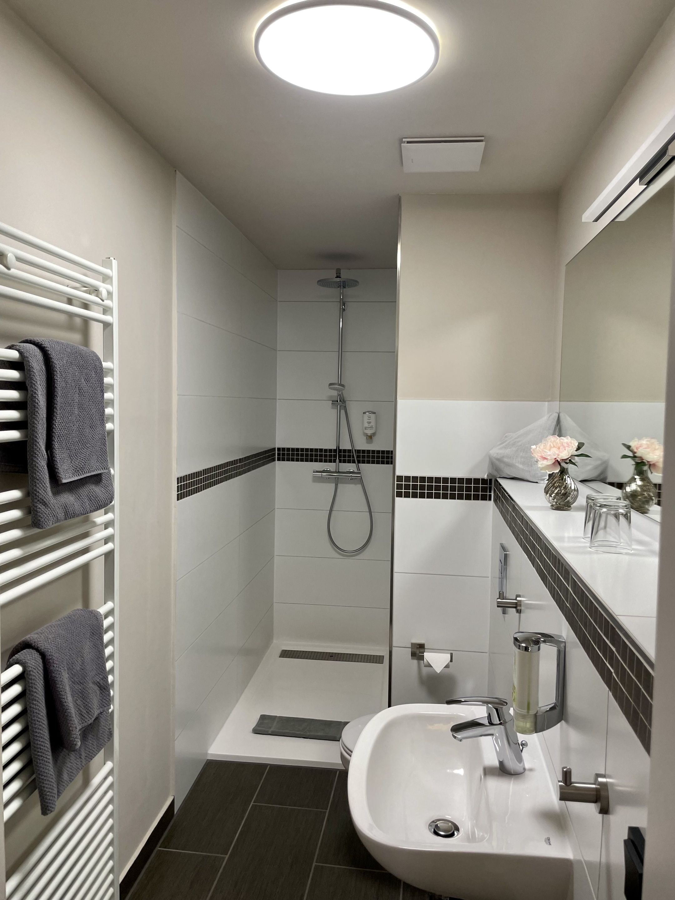 A modern bathroom with a shower, a sink, and a towel rack.