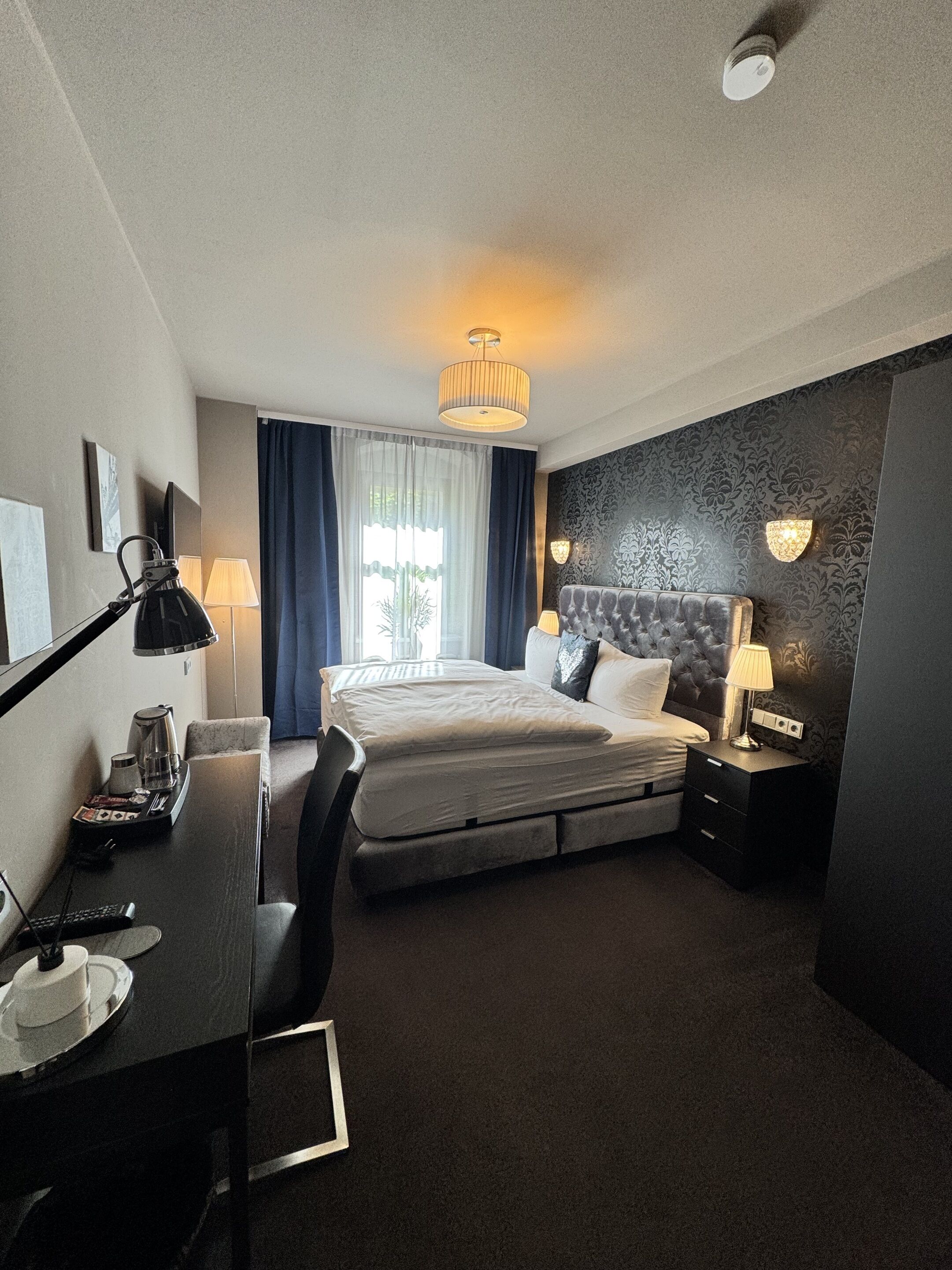 Een hotelkamer met een bed, bureau, stoel, lamp en uitzicht op de omgeving.