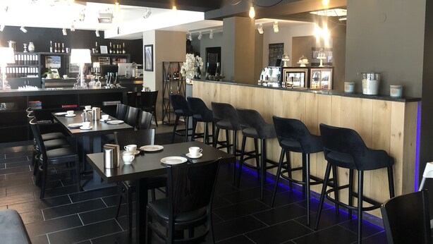 A modern bar area with a long counter, black bar stools, and a variety of bottles and glasses on shelves. - Pension Burkhardt (Meissen)