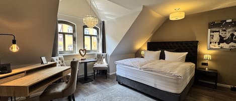 A bedroom with a bed, desk, chairs, and a chandelier.