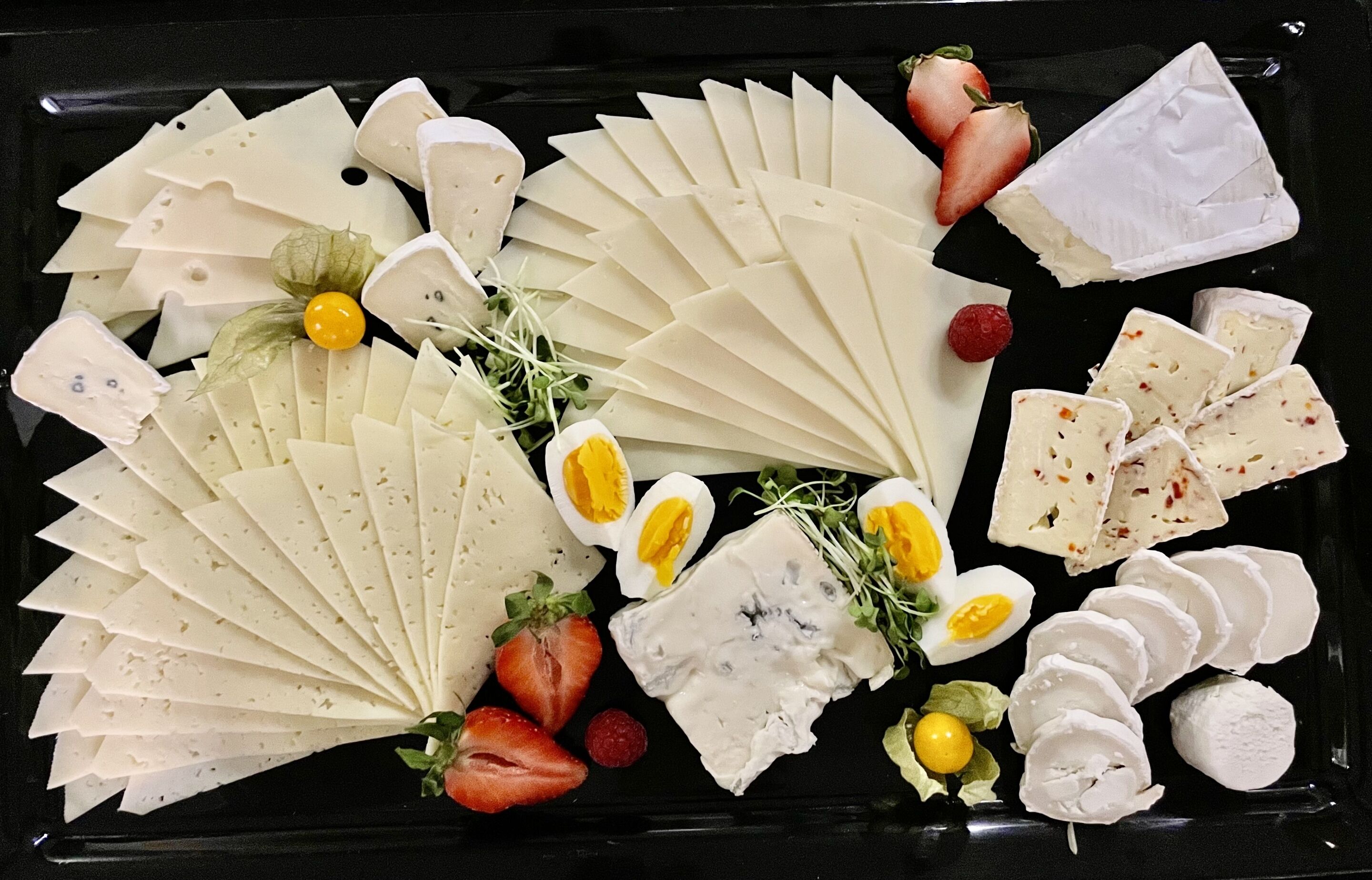 A variety of cheeses and fruits arranged on a black tray.