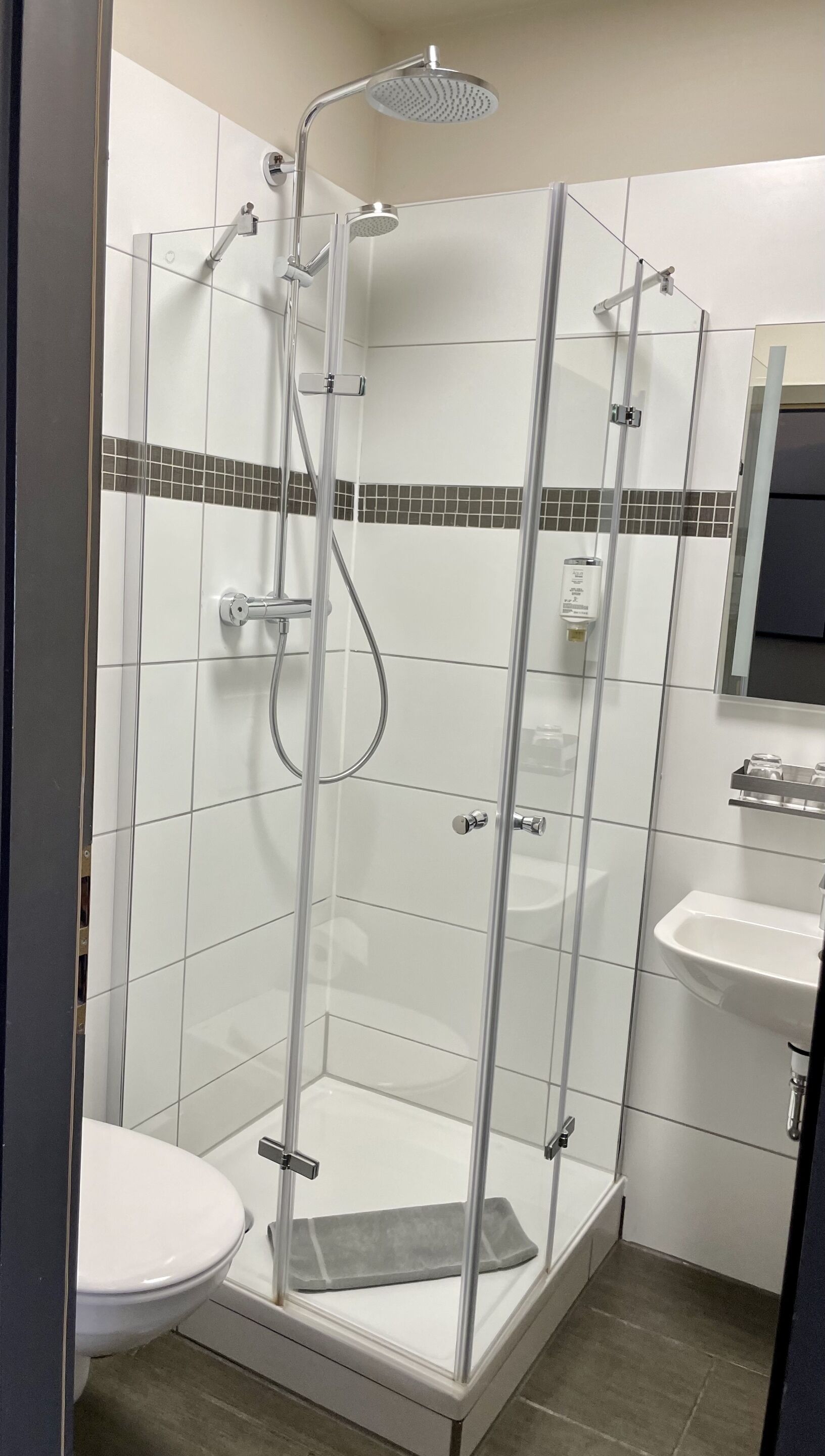 A modern bathroom with a glass-enclosed shower, white tiles, a sink, and a toilet.