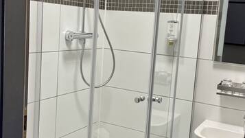 A modern bathroom with a glass-enclosed shower, white tiles, a sink, and a toilet.