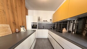 A modern kitchen with white cabinetry, a dark countertop, and a wooden accent wall. - Pension Burkhardt (Meissen)