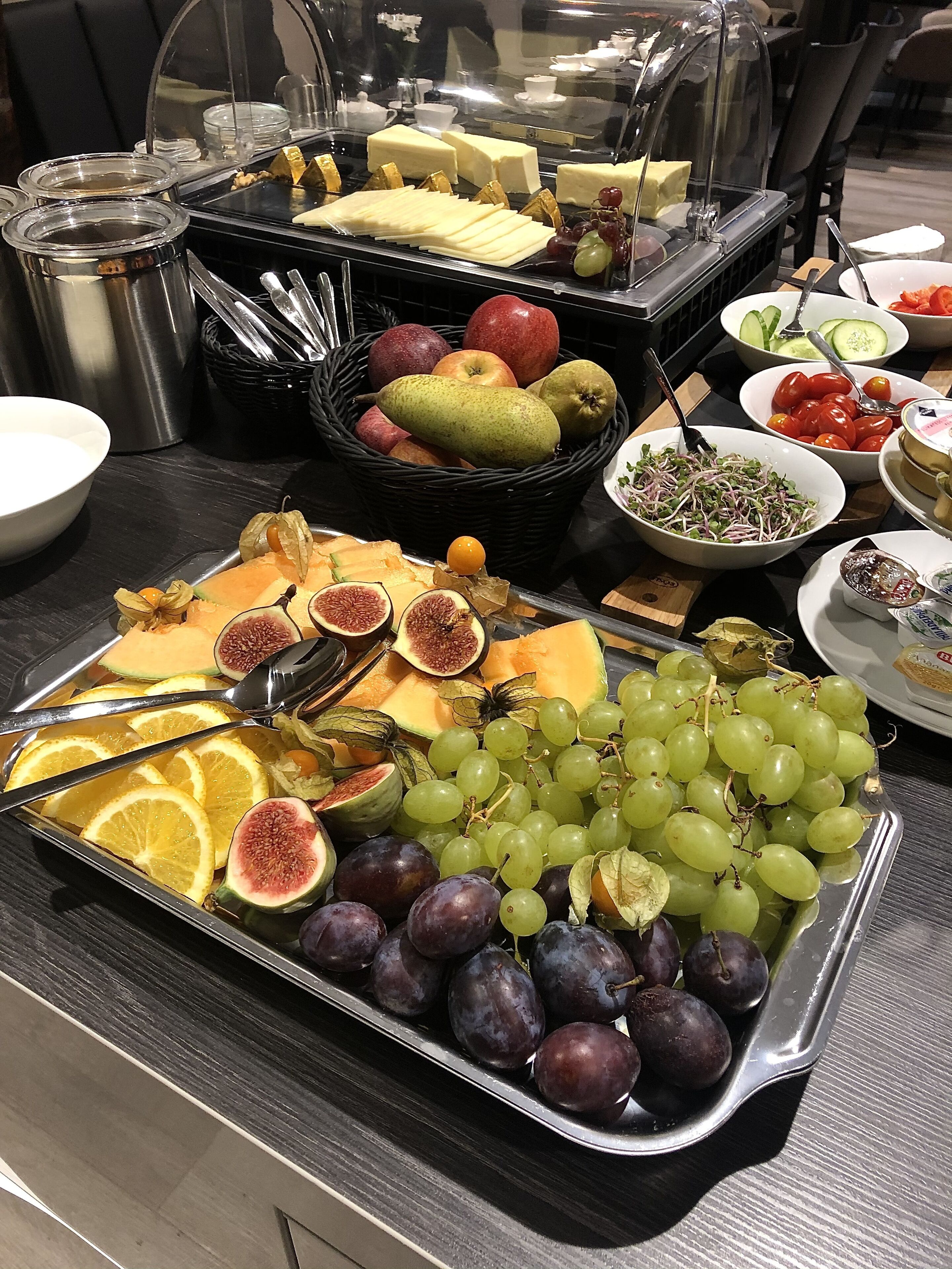 A buffet table with various fruits, cheeses, and a salad.