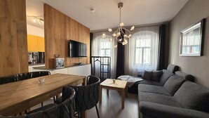A modern living room with a wooden dining table, grey sofa, and a TV mounted on the wall. - Pension Burkhardt (Meissen)