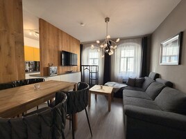 Una sala de estar moderna con una mesa de comedor de madera, un sofá gris y un televisor montado en la pared.
