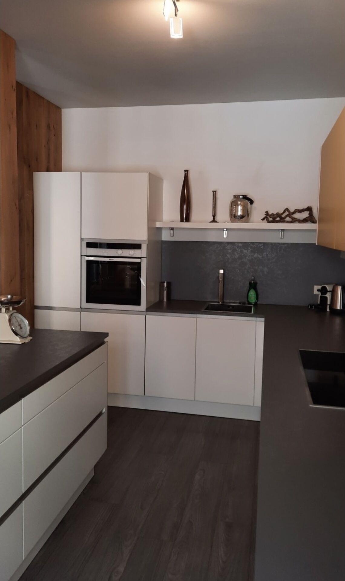 A modern kitchen with white cabinetry, a built-in oven, a sink, and a coffee machine.
