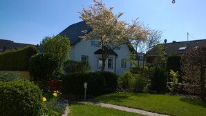 A two-story house with a dark roof, surrounded by well-maintained gardens and a lawn.