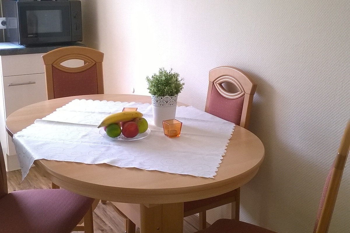 Ein Essbereich mit einem runden Tisch, Stühlen, einer Topfpflanze und einem Gemälde an der Wand.