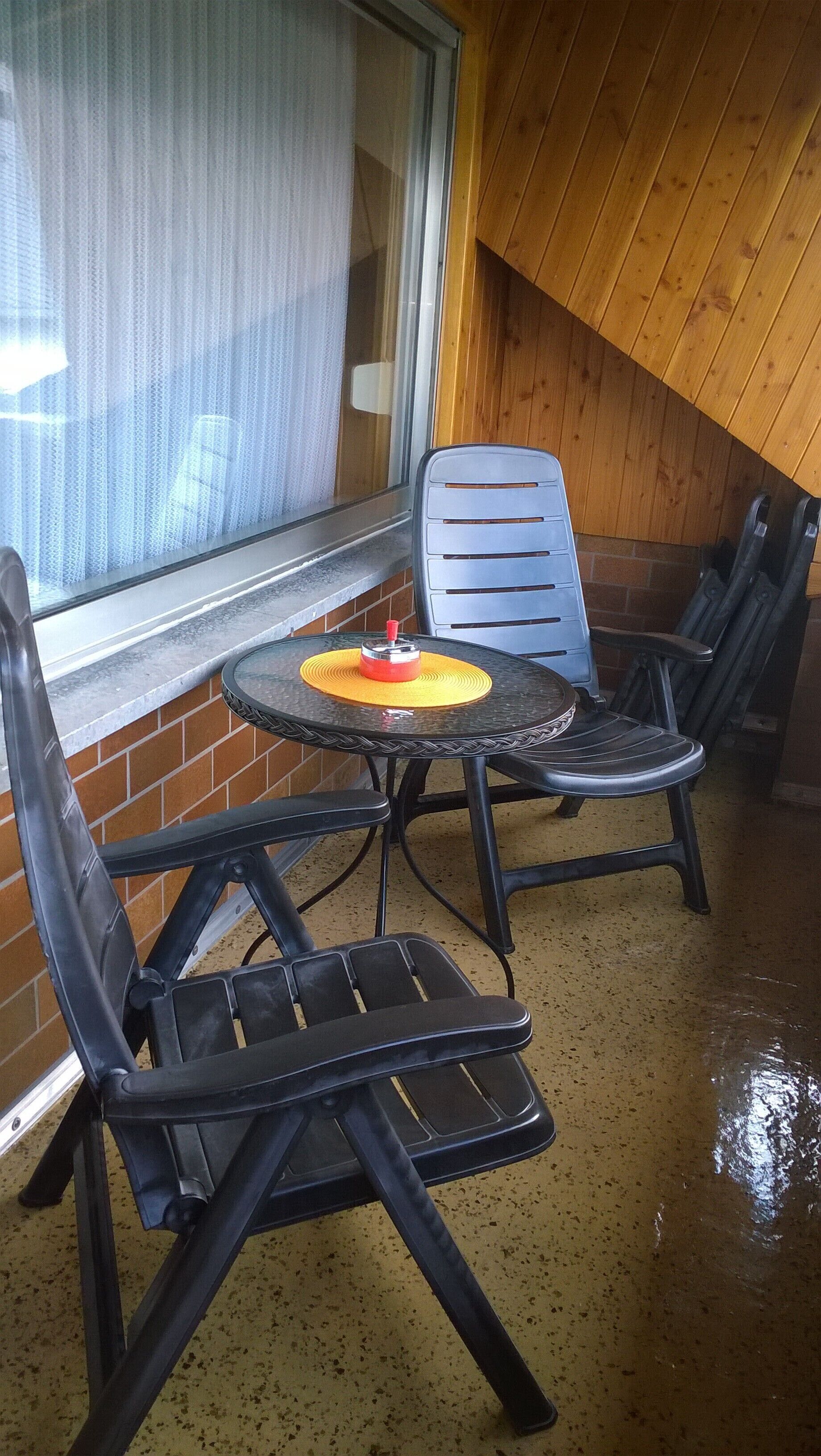 Un piccolo patio chiuso con un tavolo rotondo e due sedie, una finestra con tenda e un soffitto in legno.