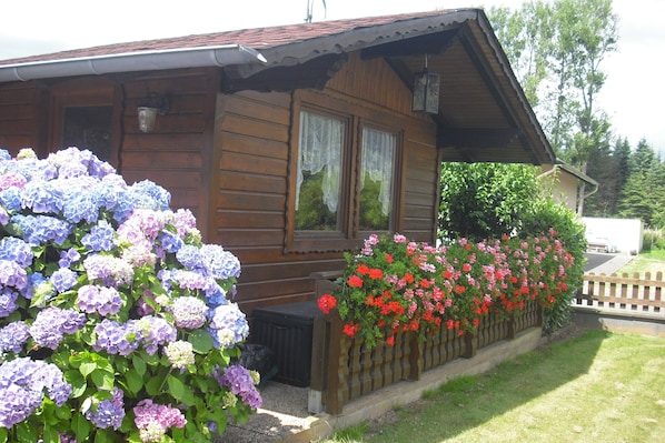 Una cabaña de madera con porche, rodeada de vibrantes flores de hortensia.