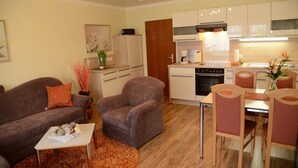 A compact living space with a sofa, armchair, dining table, and kitchenette.