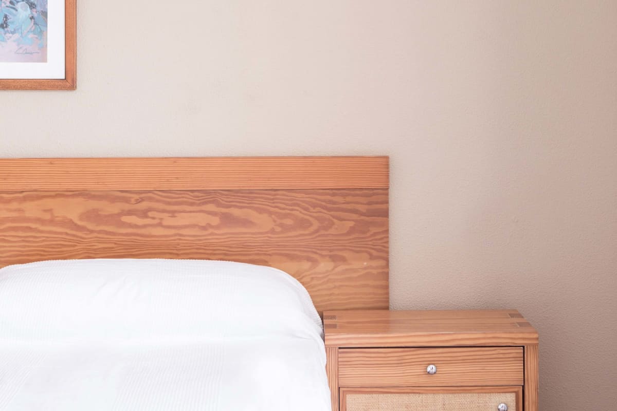 A neatly made bed with a wooden headboard, a small bedside table with a lamp, and a framed picture on the wall.