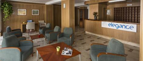Un área de recepción con un mostrador de madera, varias opciones de asiento y un cartel que dice "elegance".