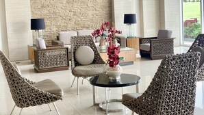 Un área de estar moderna con mobiliario de mimbre, una mesa de centro de cristal y una pared de piedra.