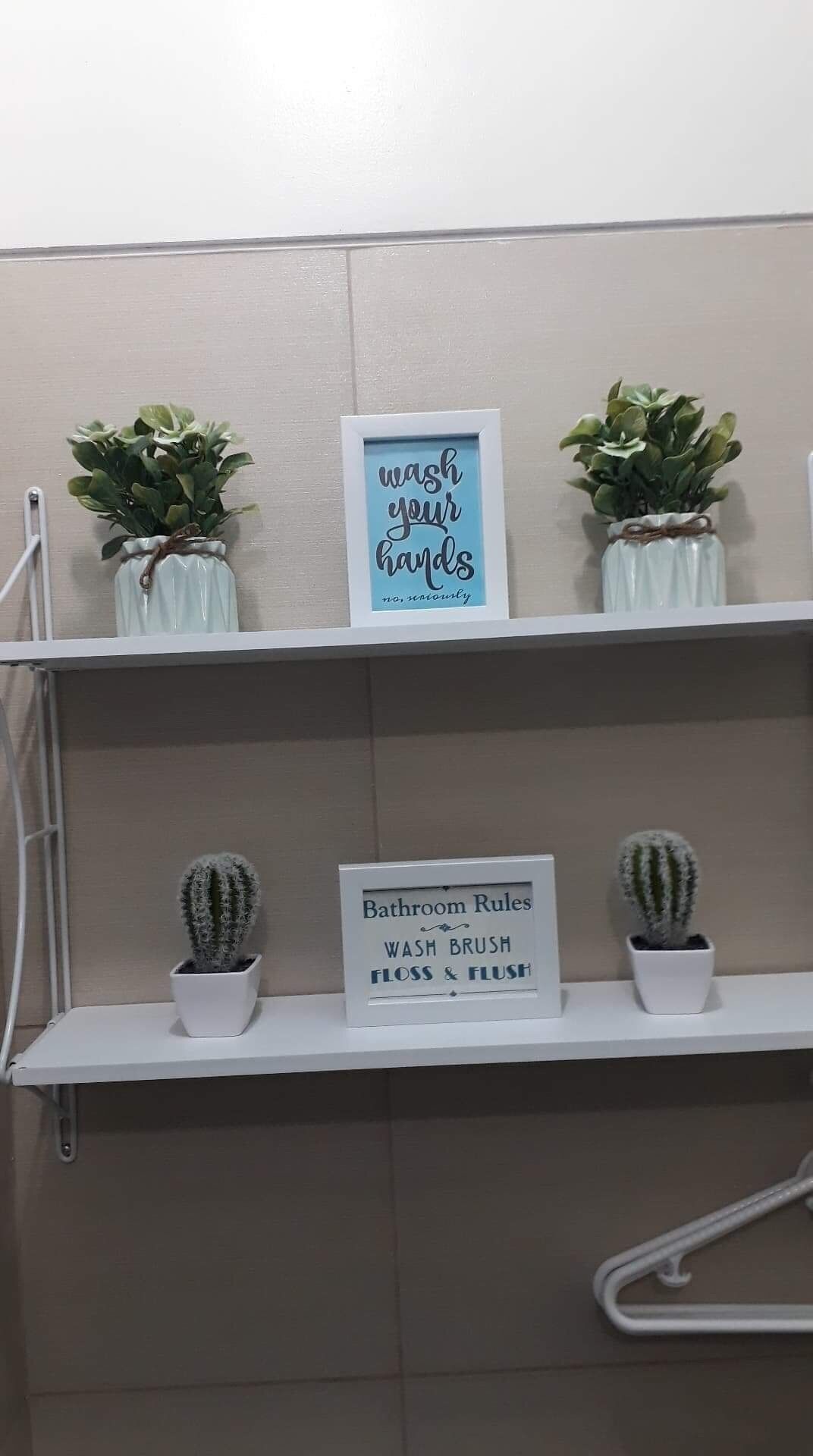 A bathroom with a sign that reads "wash your hands no, unnecessarily" and another sign that says "Bathroom Rules: WASH BRUSH FLOSS & FLUSH". There are two potted plants on the shelf above the signs.