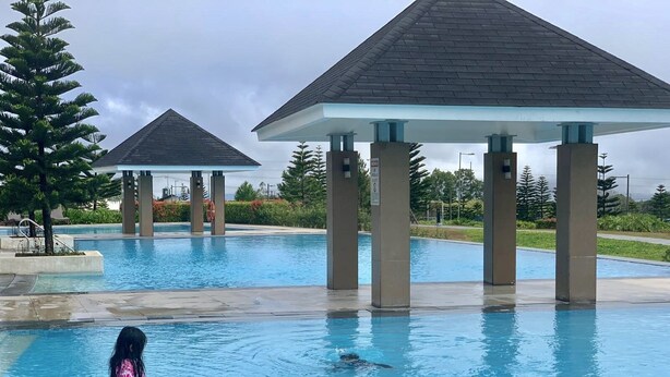 Una piscina con dos gazebos, un puesto de socorrista y una persona nadando.