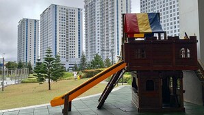 Un parque infantil con un tobogán y una pequeña estructura de ladrillo, rodeado de altos edificios residenciales.