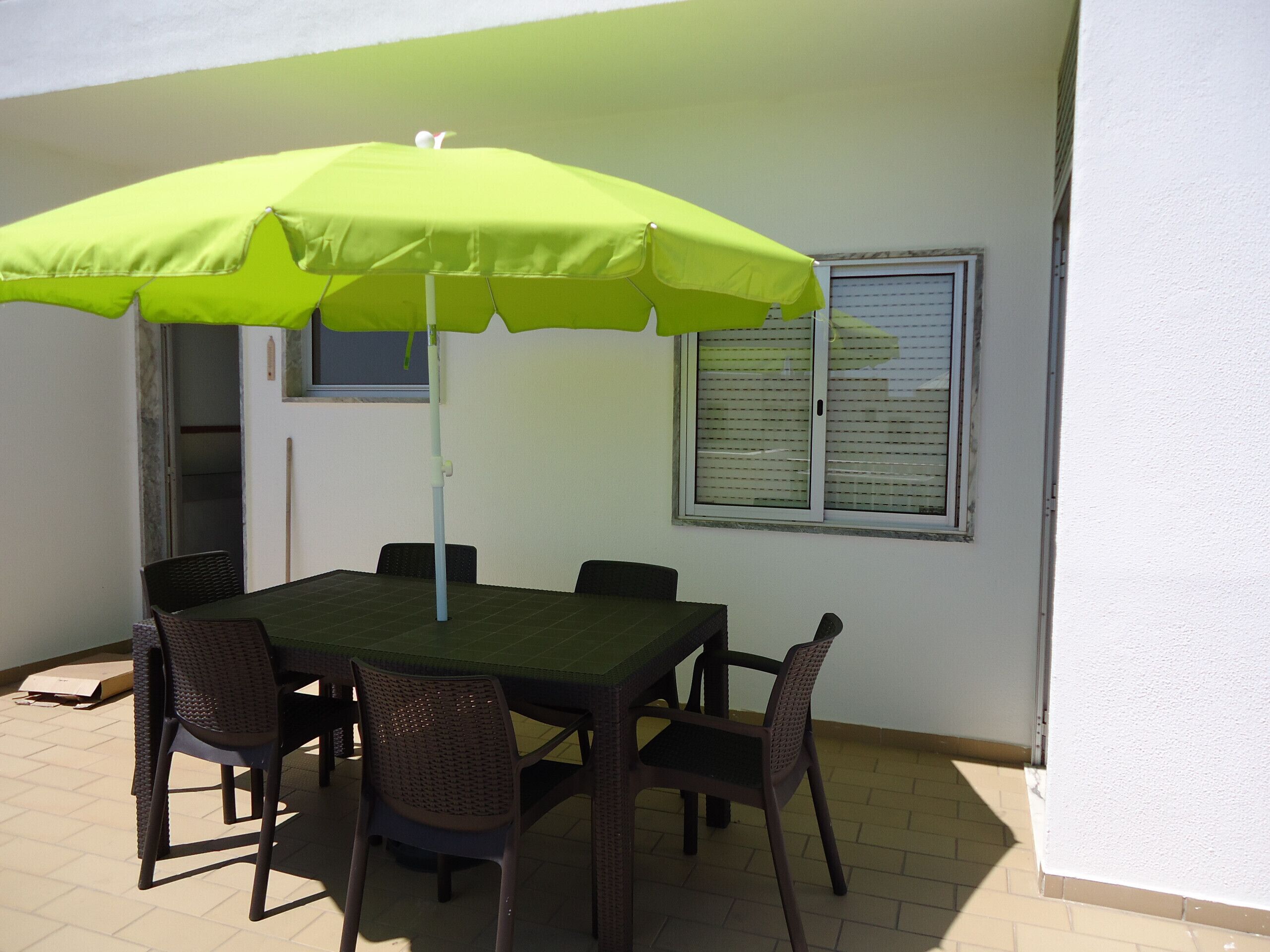 Une terrasse avec une table et des chaises, un parasol et une fenêtre avec des stores.