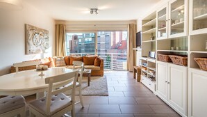 A modern living room with a dining area, large windows, and a view of buildings. - Gaston Lejeune 304 (Koksijde)