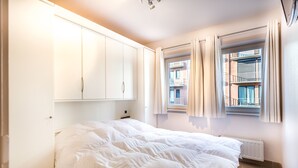 A bedroom with a bed, a wardrobe, a radiator, and a window with curtains. - Gaston Lejeune 304 (Koksijde)