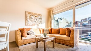 A modern living room with wicker furniture, a large window, and a city view. - Gaston Lejeune 304 (Koksijde)