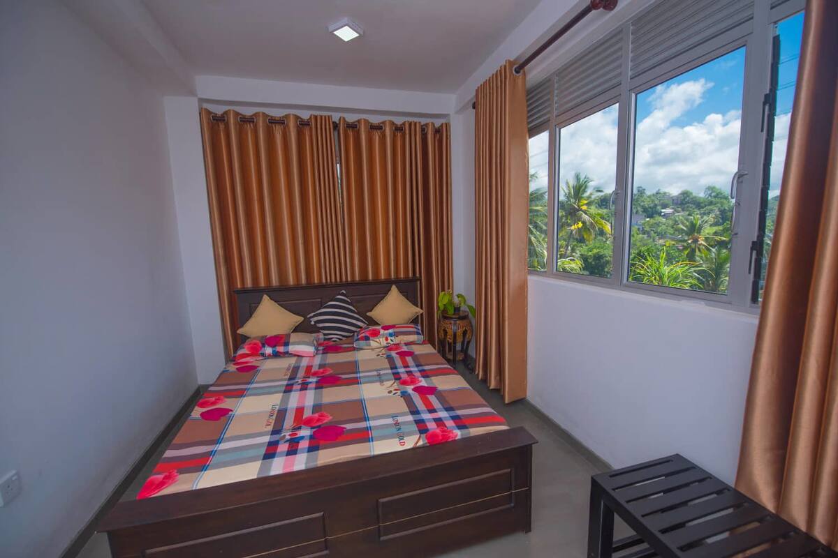 A bedroom with a bed, curtains, a window with a view, and a small table.