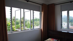 Un dormitorio con cama, ventana con persianas y vista a la vegetación.