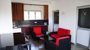 Una habitación de hotel moderna con kitchenette, una zona de comedor con mesa y sillas, y un rincón de descanso con sillas rojas y negras.